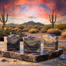 Three bars of soap on a wooden platform with a desert landscape and sunset in the background.