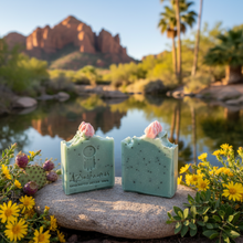 Two green soaps with pink flowers on a rock by a desert landscape with mountains and a lake.