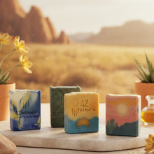 Four soap bars with desert-themed designs on a wooden surface with a blurred desert landscape in the background.